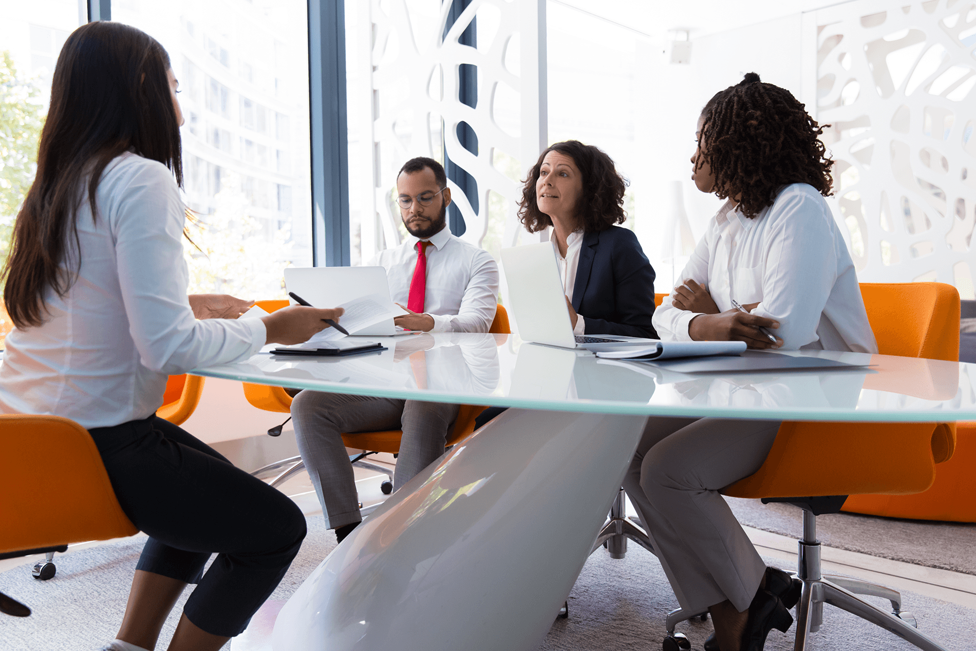 Corporate meeting room where a woman is being interviewed at the edge of her seat by 3 hiring executives.